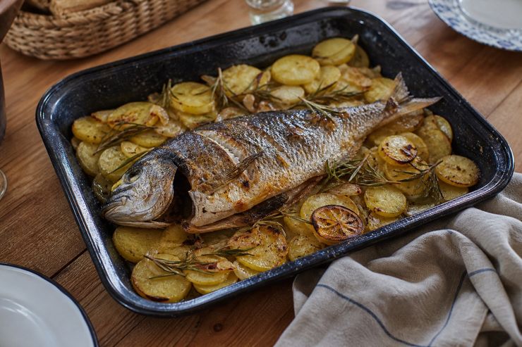 Pescado de roca entero asado con patatas, limón y romero en una bandeja de horno